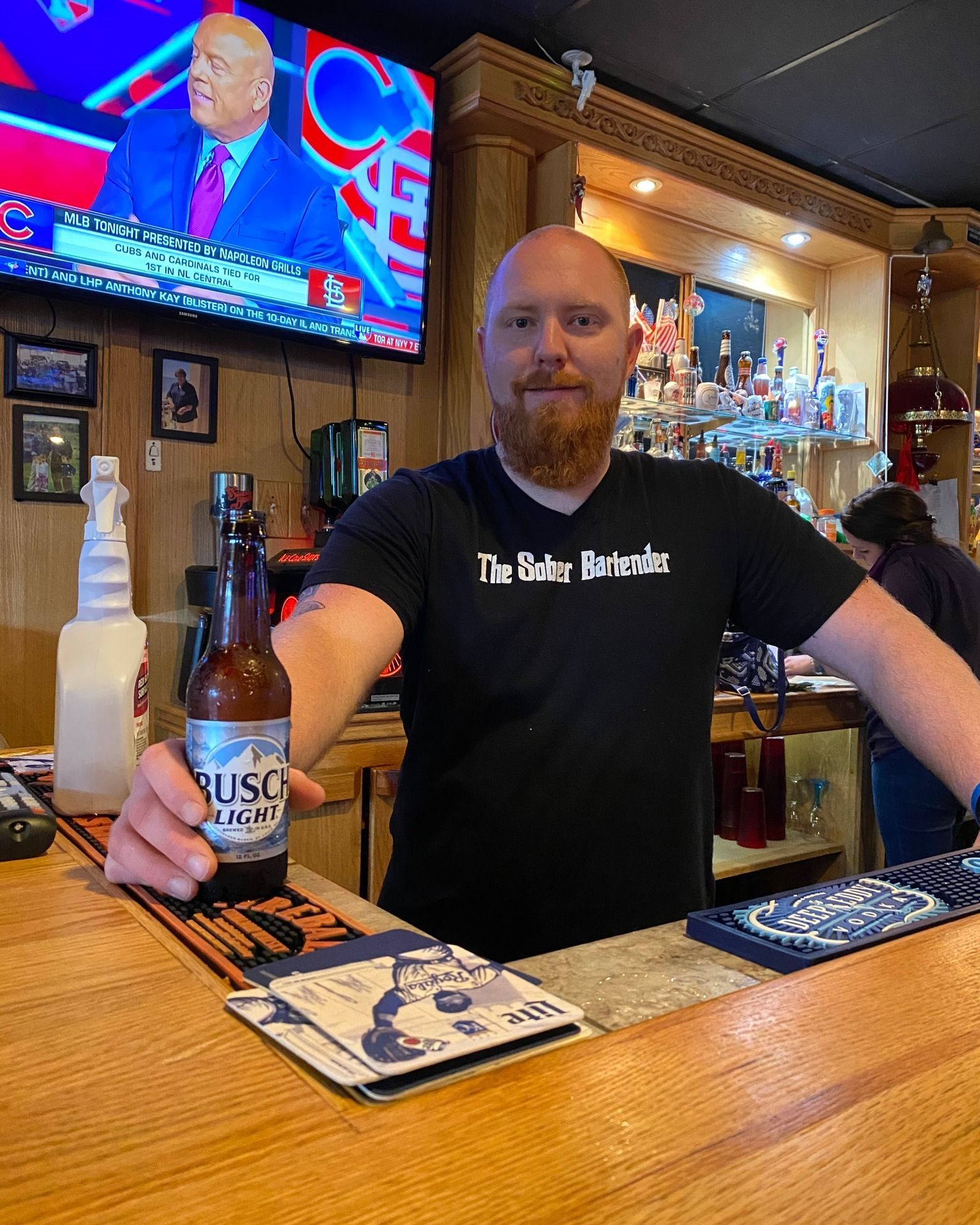 A man is standing at a bar holding a bottle of beer.