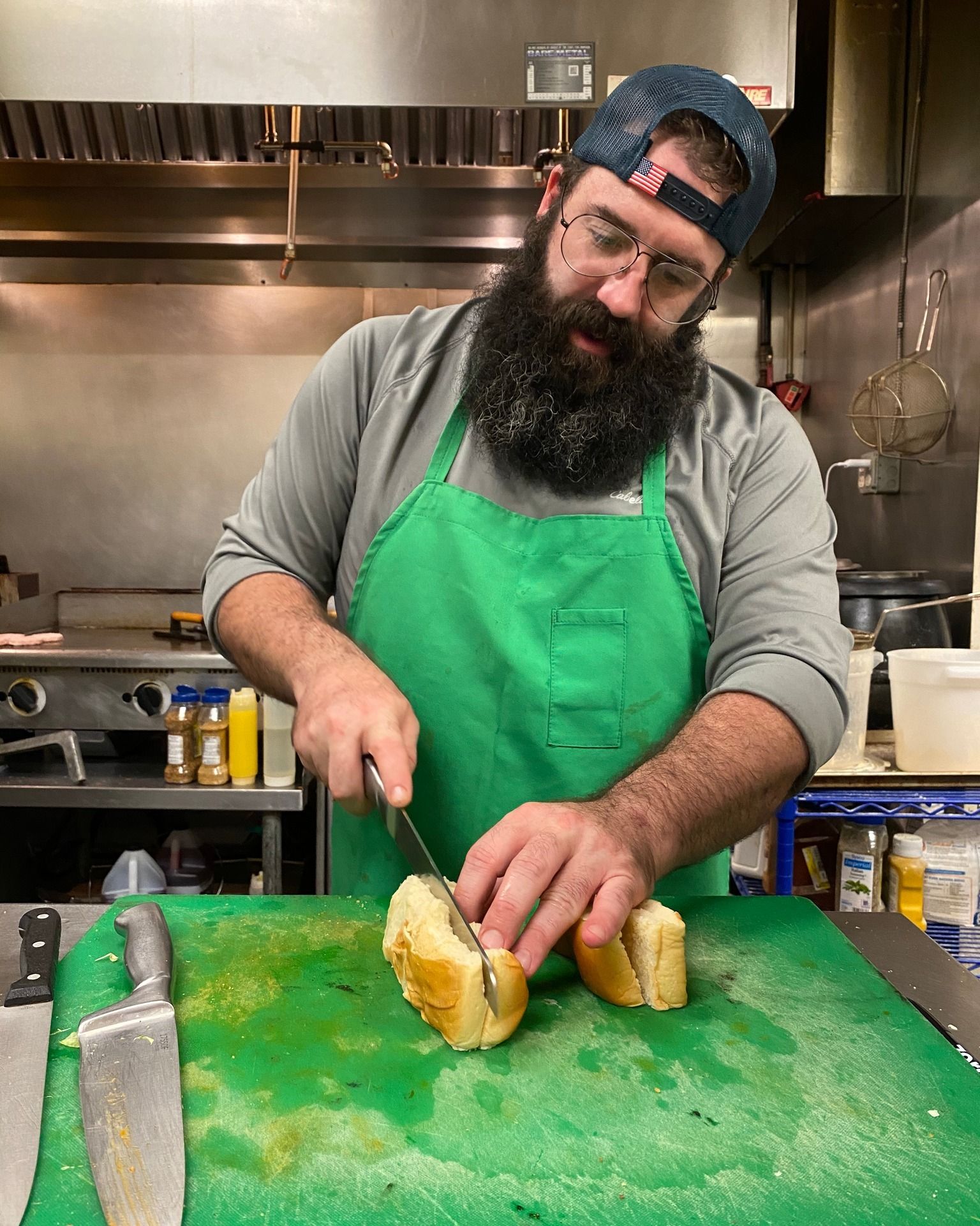 A man with a beard is cutting a hot dog on a cutting board.
