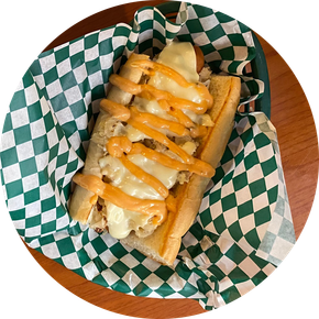 A hot dog with cheese and sauce on a checkered paper on a plate.