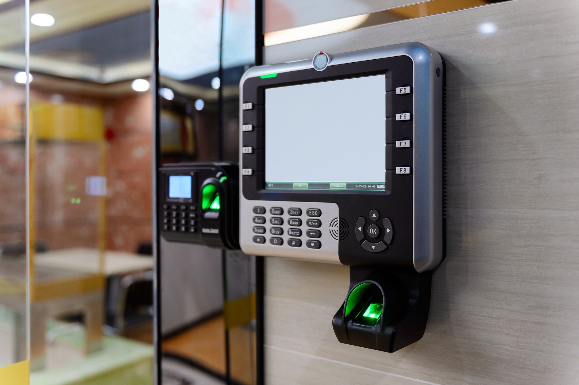 A fingerprint scanner is mounted on a wall next to a glass door.