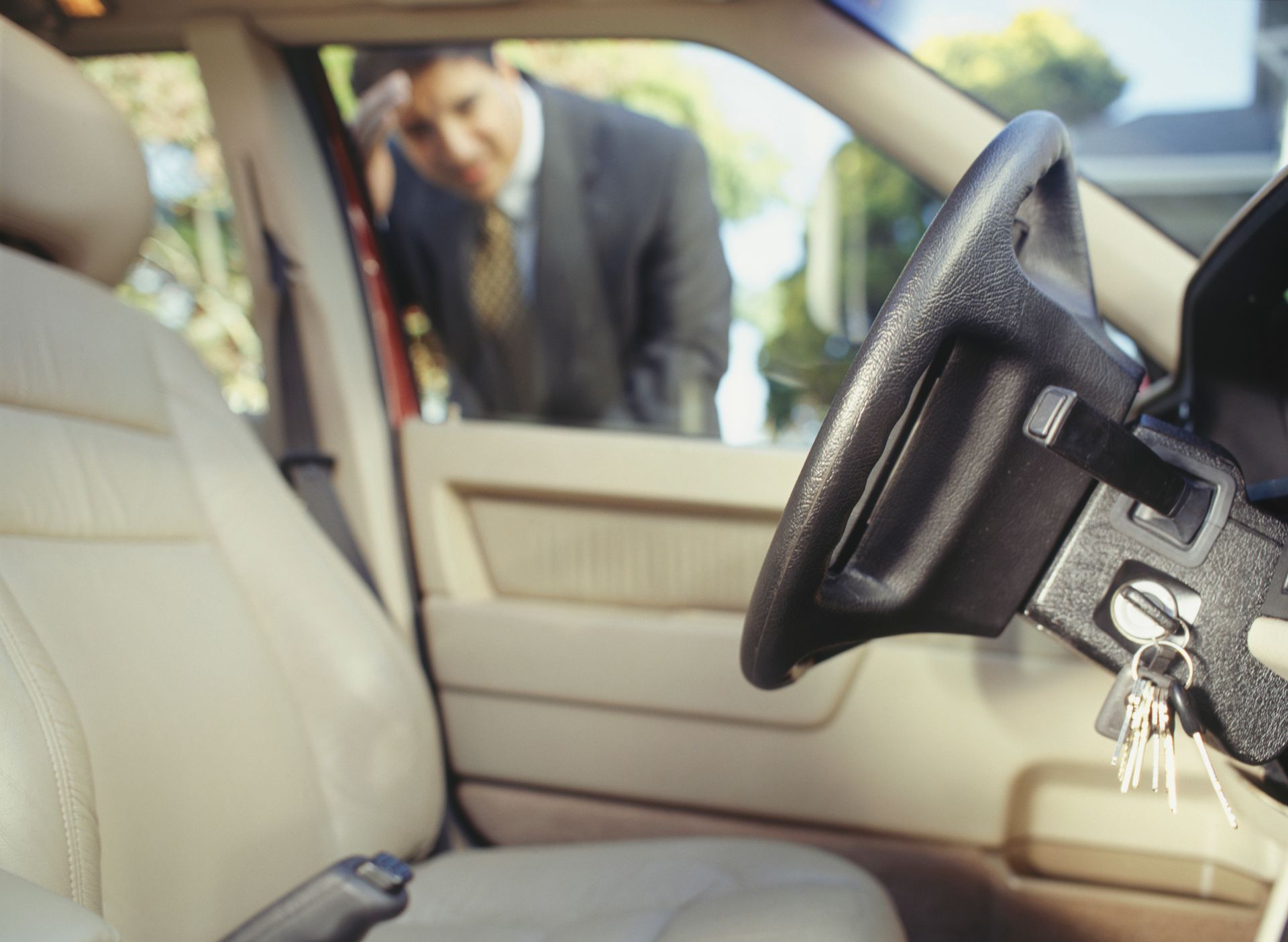 A man in a suit is looking through the window of a locked car.