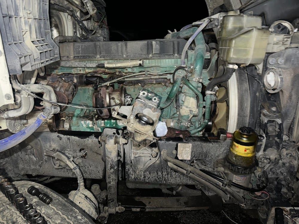 Damaged car engine bay with exposed green engine components and disconnected hoses