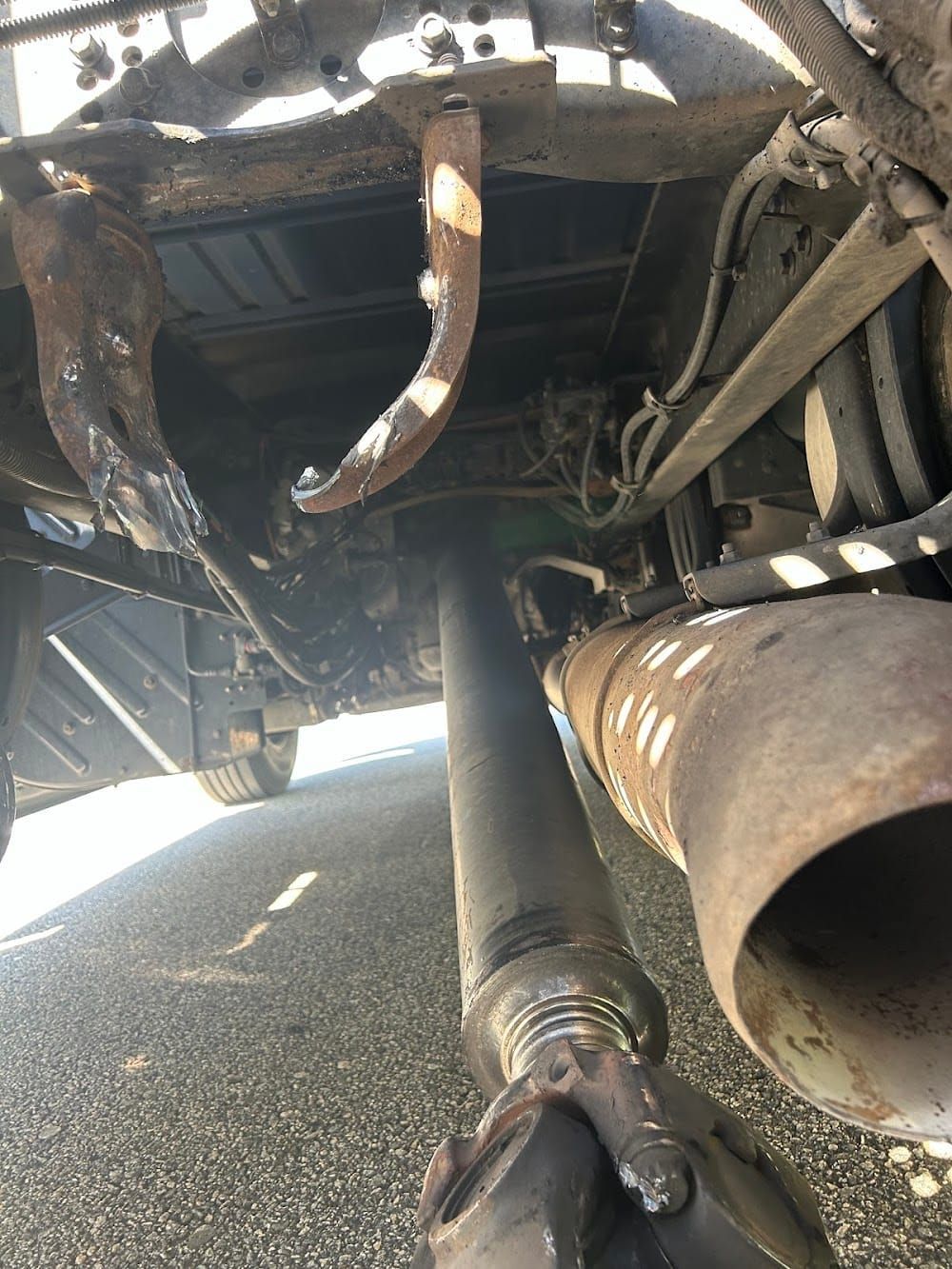 Undercarriage of a vehicle with exhaust pipe, suspension parts, and a driveshaft visible on pavement.