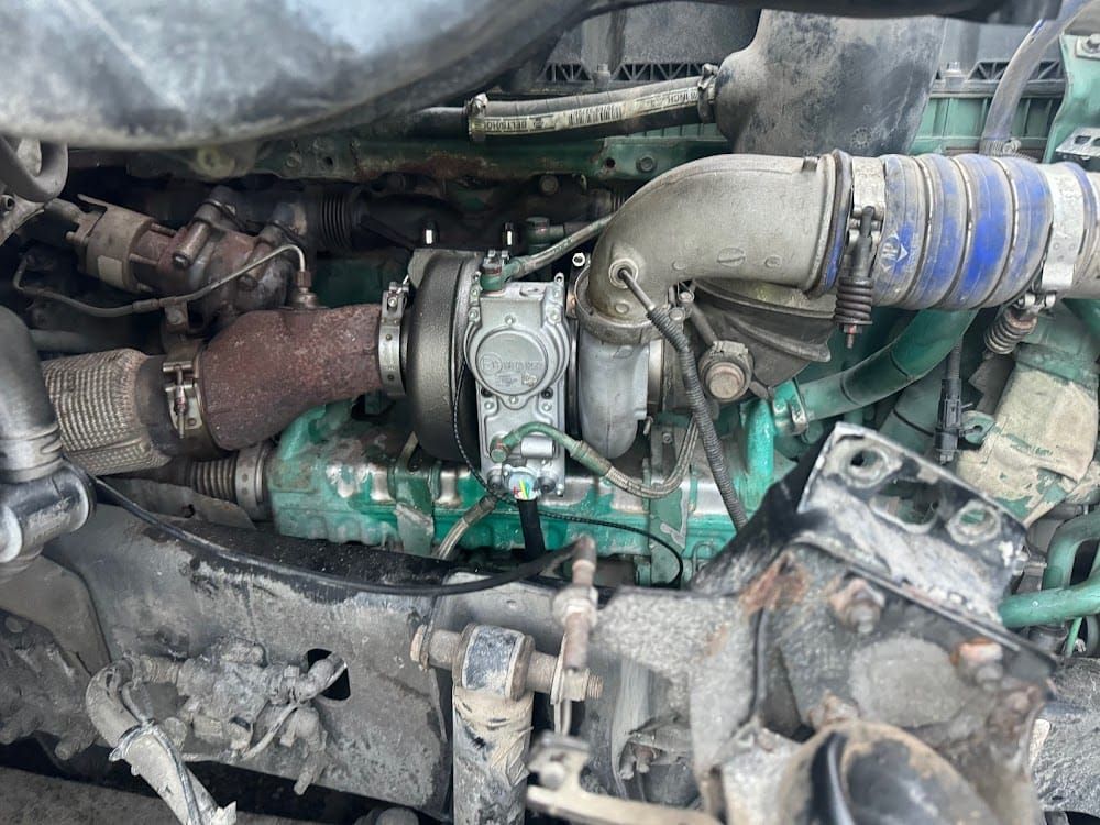 Close-up of a dirty vehicle engine with hoses, pipes, and a turbocharger assembly under the hood