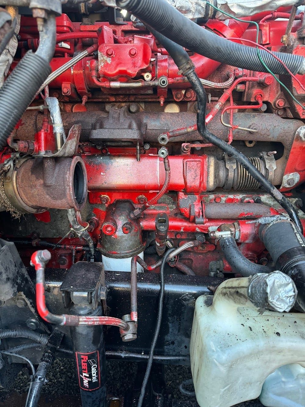 Close-up of a red engine compartment with hoses, pipes, and a white plastic fluid tank