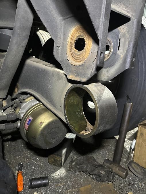 Close-up of a car’s rear suspension and exhaust area with a rusted mounting hole and loose parts nearby