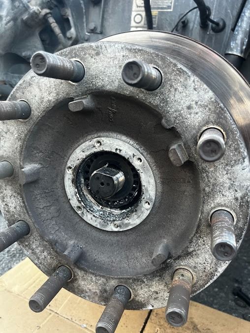 Close-up of a rusty vehicle wheel hub with six lug studs and a central axle opening