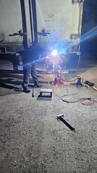 Person welding near a truck at night, bright sparks illuminating tools on the ground.