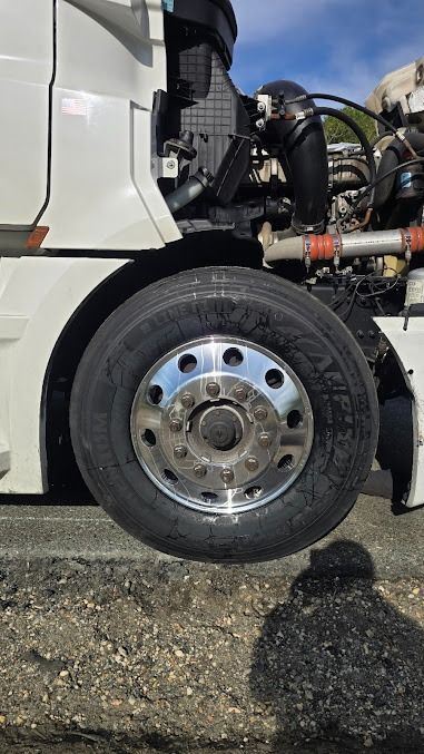Close-up of a truck’s front wheel and exposed engine components on a road shoulder