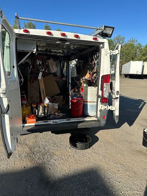 Open utility van with rear doors open, showing tools and supplies inside in a gravel lot.