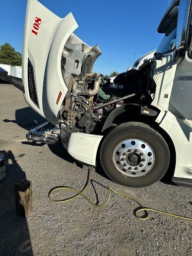 White semi-truck with hood open, exposing engine damage after a roadside collision.
