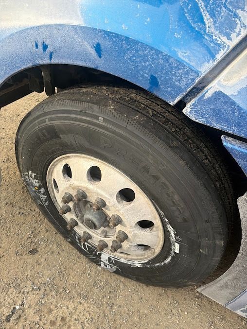 Close-up of a blue vehicle’s dirty front wheel and rim on a sandy surface