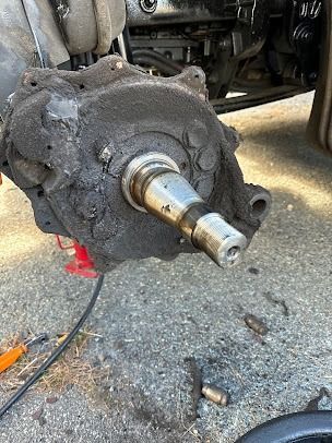Damaged vehicle axle and hub assembly with exposed metal shaft on gravel ground