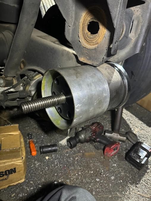 Close-up of a disassembled mechanical part with tools on the floor, showing a metal cylinder and exposed bolt.