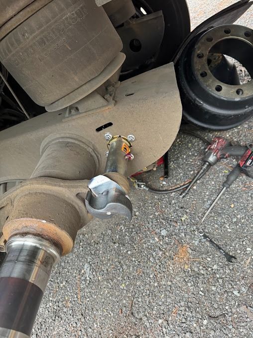 Brake rotor and suspension parts exposed beside a wheel on a car, with tools on the pavement.