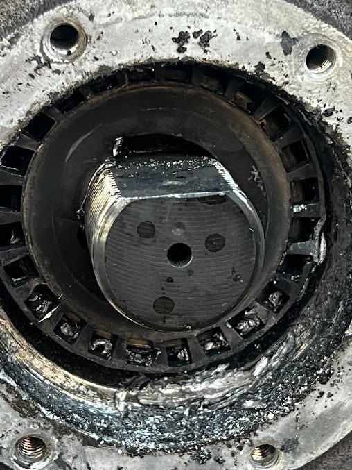Close-up of a corroded metal pipe fitting with a central hex bolt and circular flange holes