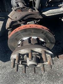 Vehicle wheel hub and brake rotor with exposed lug bolts, showing rust and wear on a car axle