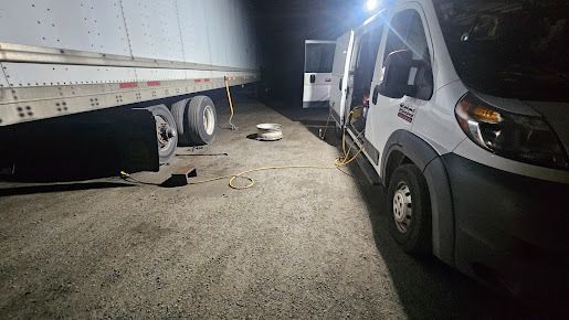 Truck and trailer parked on gravel at night, lit by bright vehicle headlights