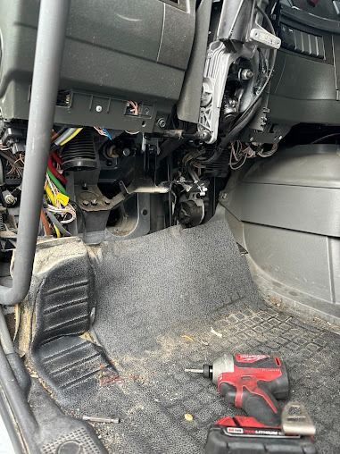 Car interior with exposed dashboard wiring and a red tool on the floor mat