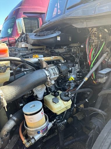 Close-up of a truck engine bay with exposed hoses, filters, and mechanical parts under the hood