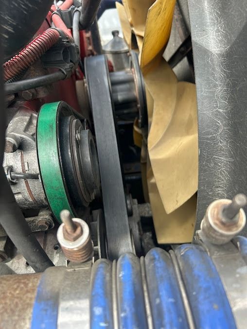 Close-up of engine belts, pulleys, and a yellow cooling fan in a mechanical compartment
