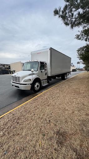 White box truck parked on a roadside shoulder beside a grassy embankment under a cloudy sky