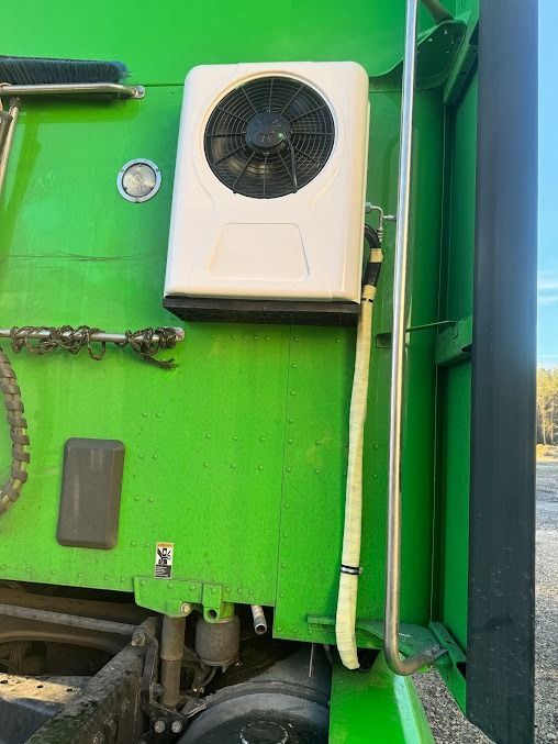 White wall-mounted air conditioner on a bright green vehicle side with cables and metal hardware.