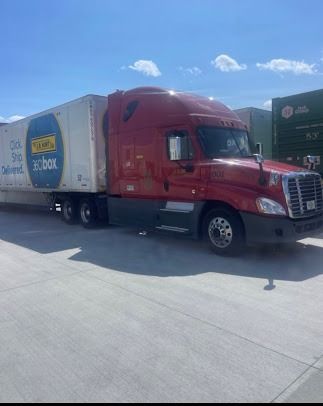 Red semi-truck with trailer parked on a sunny lot under a blue sky