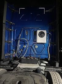 Blue truck cab interior with exposed hoses, wiring, and a small fan unit mounted on the back wall
