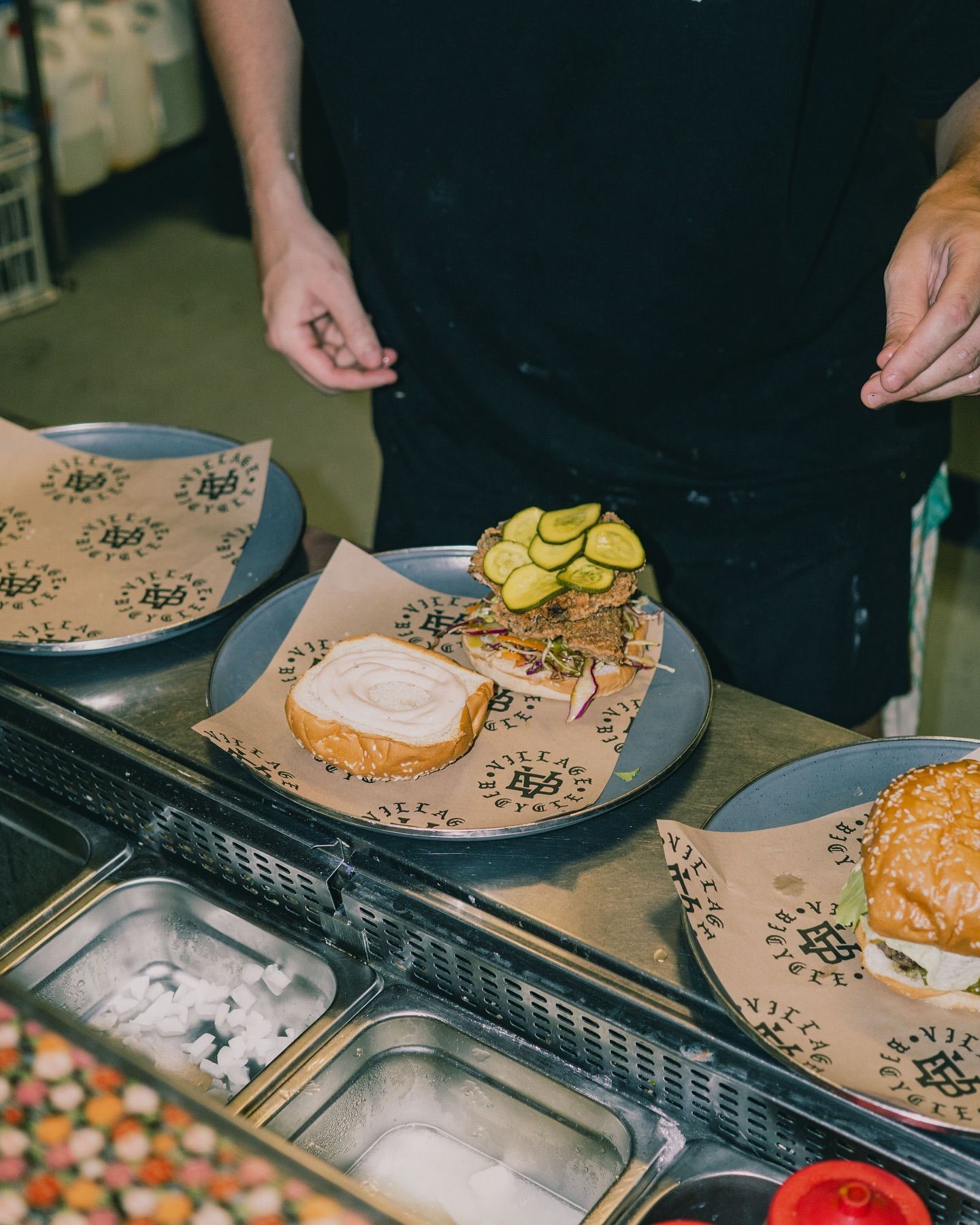 A Person Assembling a Burger on a Counter — Village Bicycle Noosa in Noosa Heads, QLD