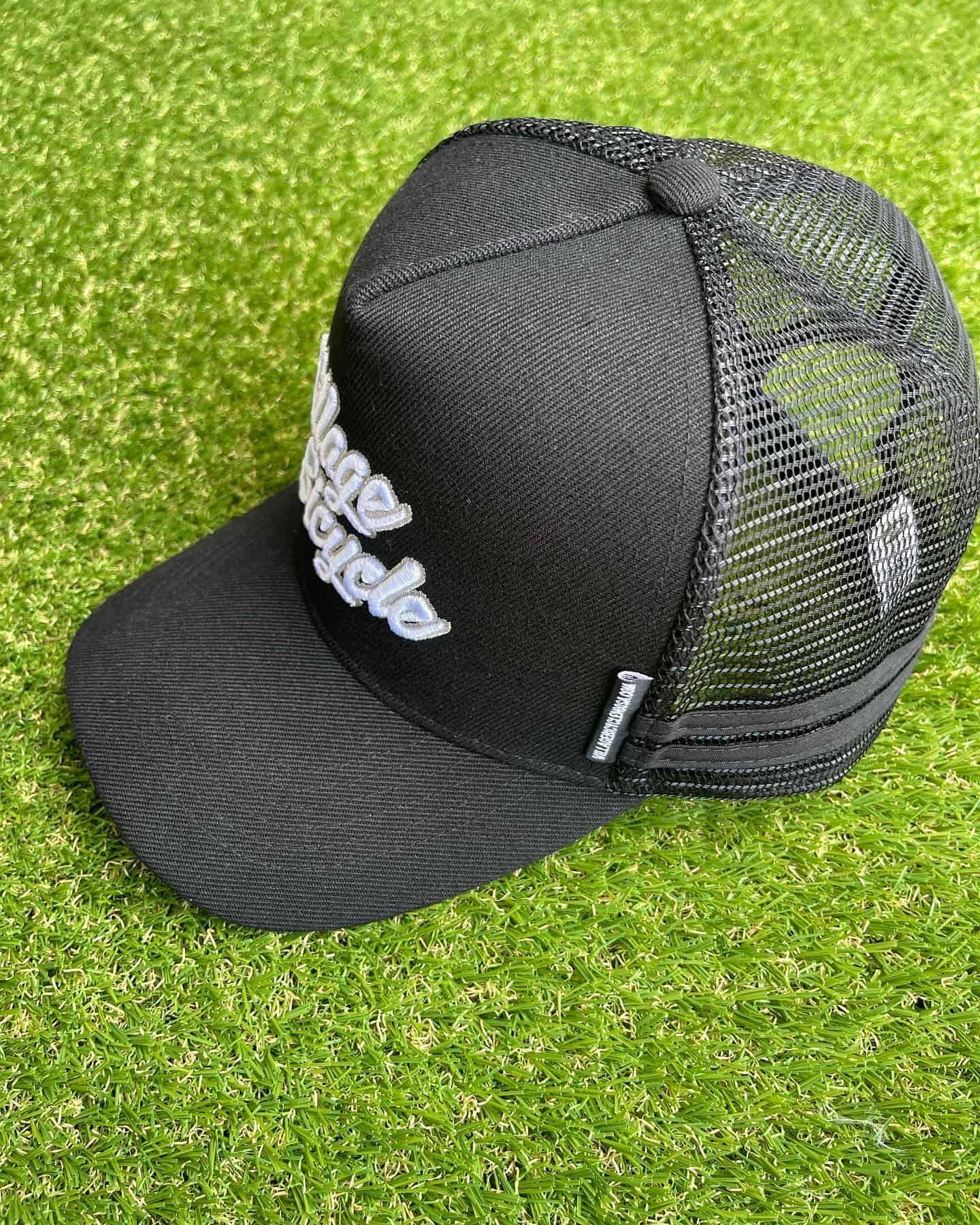 Black trucker hat with white text on green grass.
