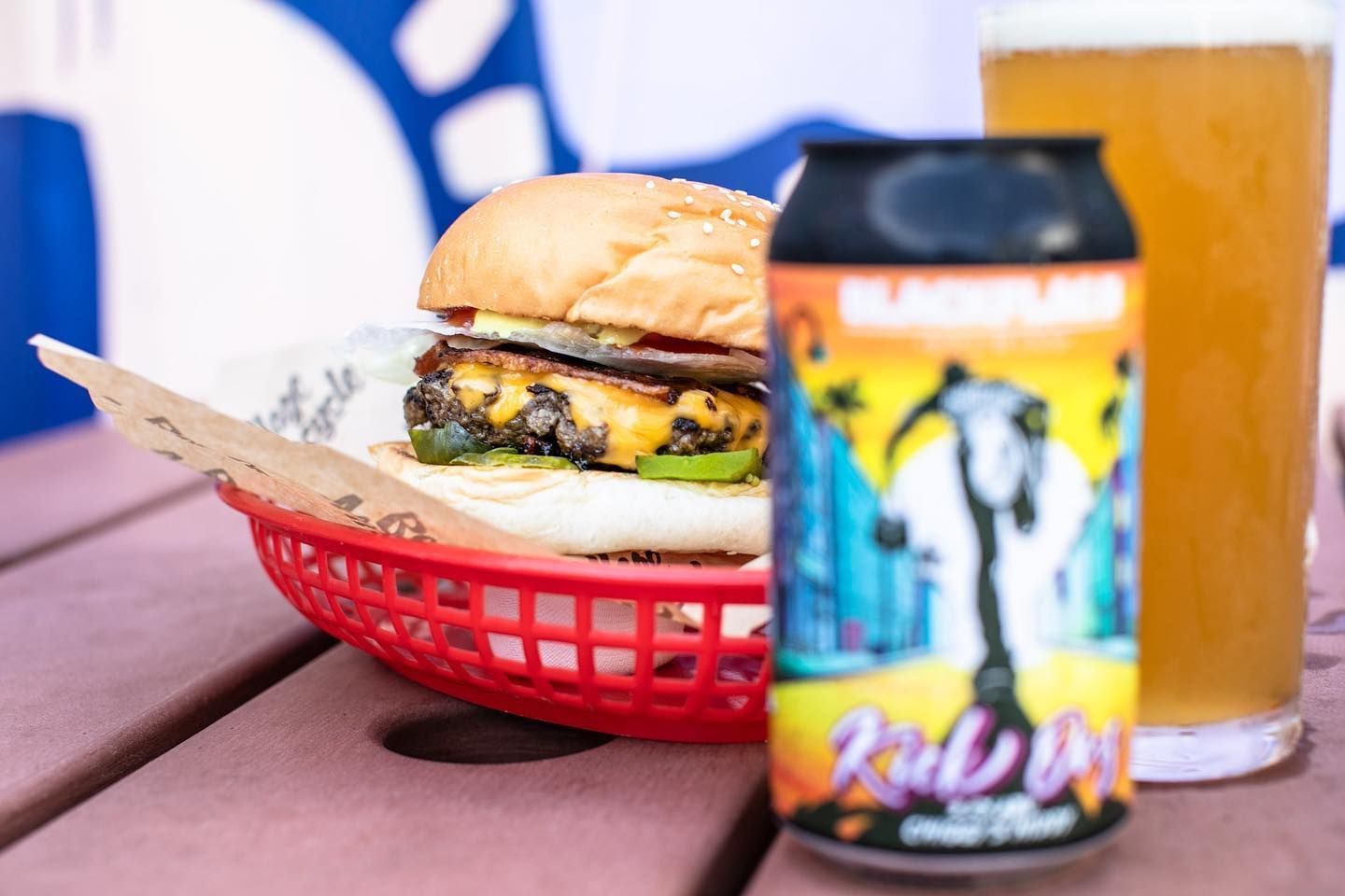 Burger in Red Basket With Beer Can and Pint Glass on Pink Table — Village Bicycle Noosa in Noosa Heads, QLD