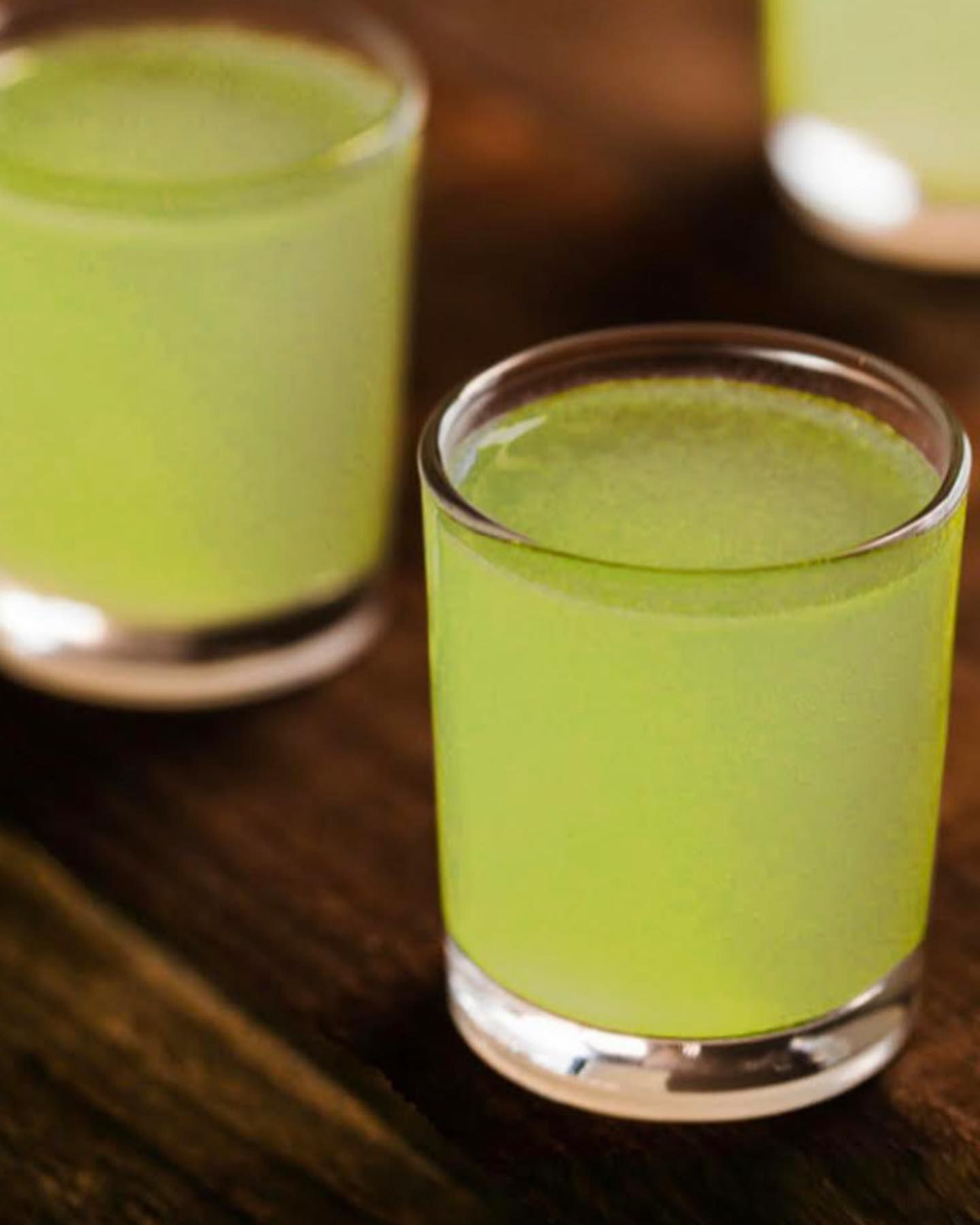 Three Shot Glasses Filled With a Bright Green Liquid, on a Wooden Surface — Village Bicycle Noosa in Noosa Heads, QLD