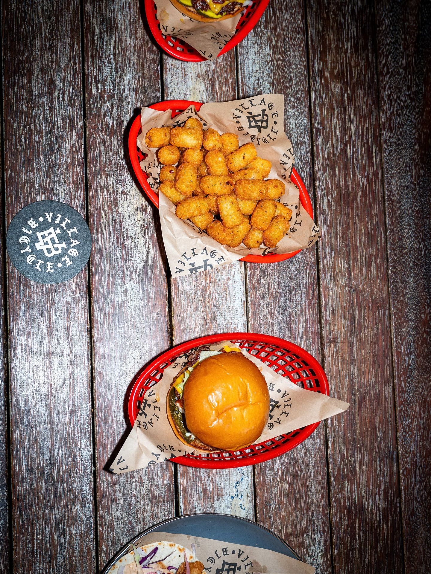 Burgers, tater tots, and a coaster on a wooden table, in red baskets — Village Bicycle Noosa in Noosa Heads, QLD