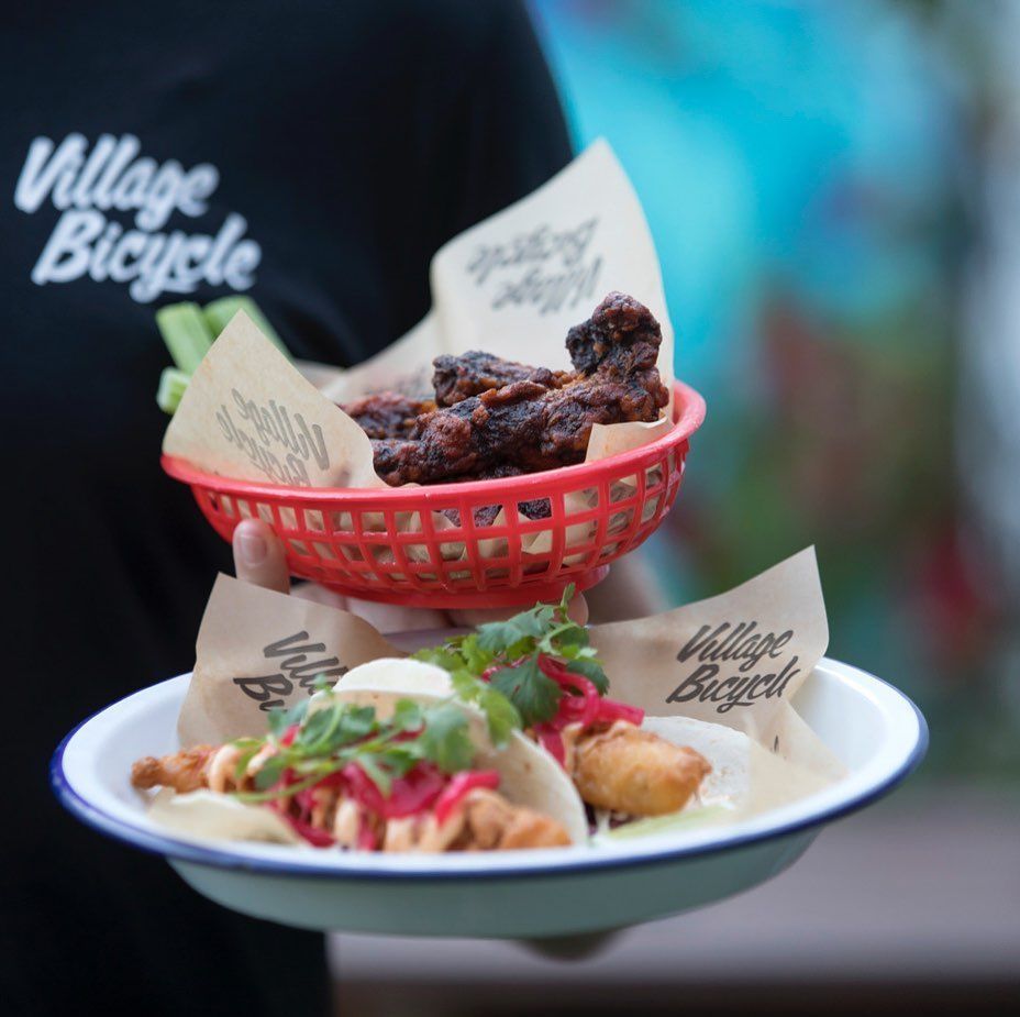Person Holding Red Basket With Chicken Wings and Plate With Tacos — Village Bicycle Noosa in Noosa Heads, QLD