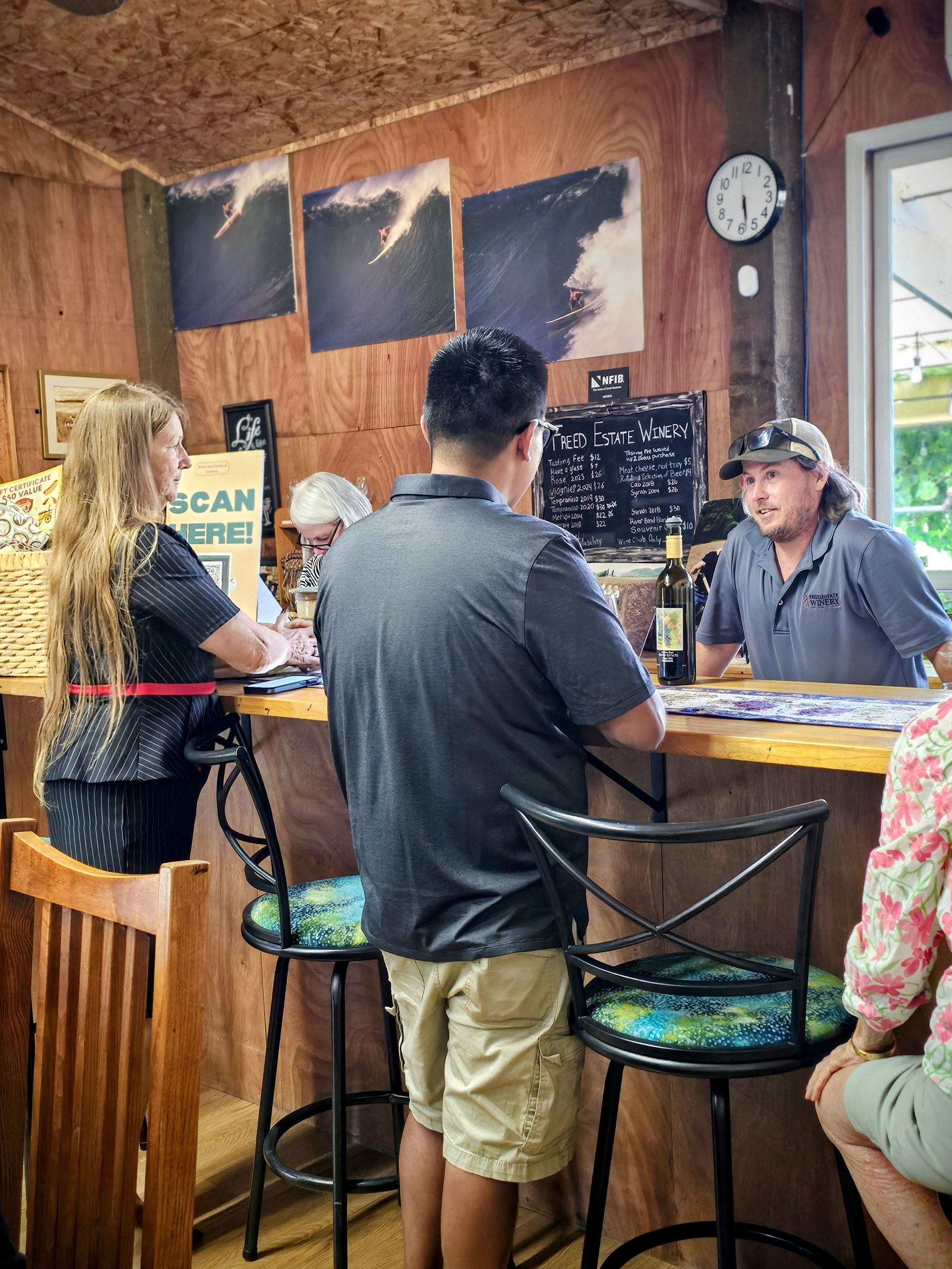People at a bar; woman seated at counter, man talking to a bartender, wooden interior, wave art.