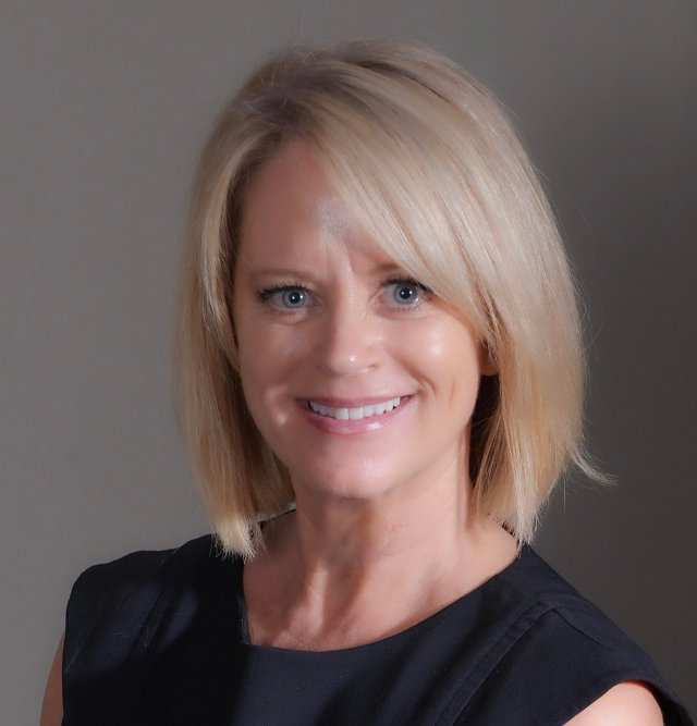 A woman with blonde hair and blue eyes is smiling for the camera