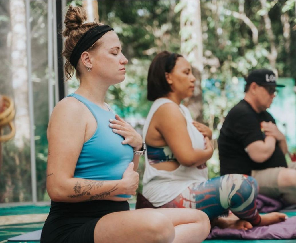 A group of people are sitting on a yoga mat with their hands on their chests.