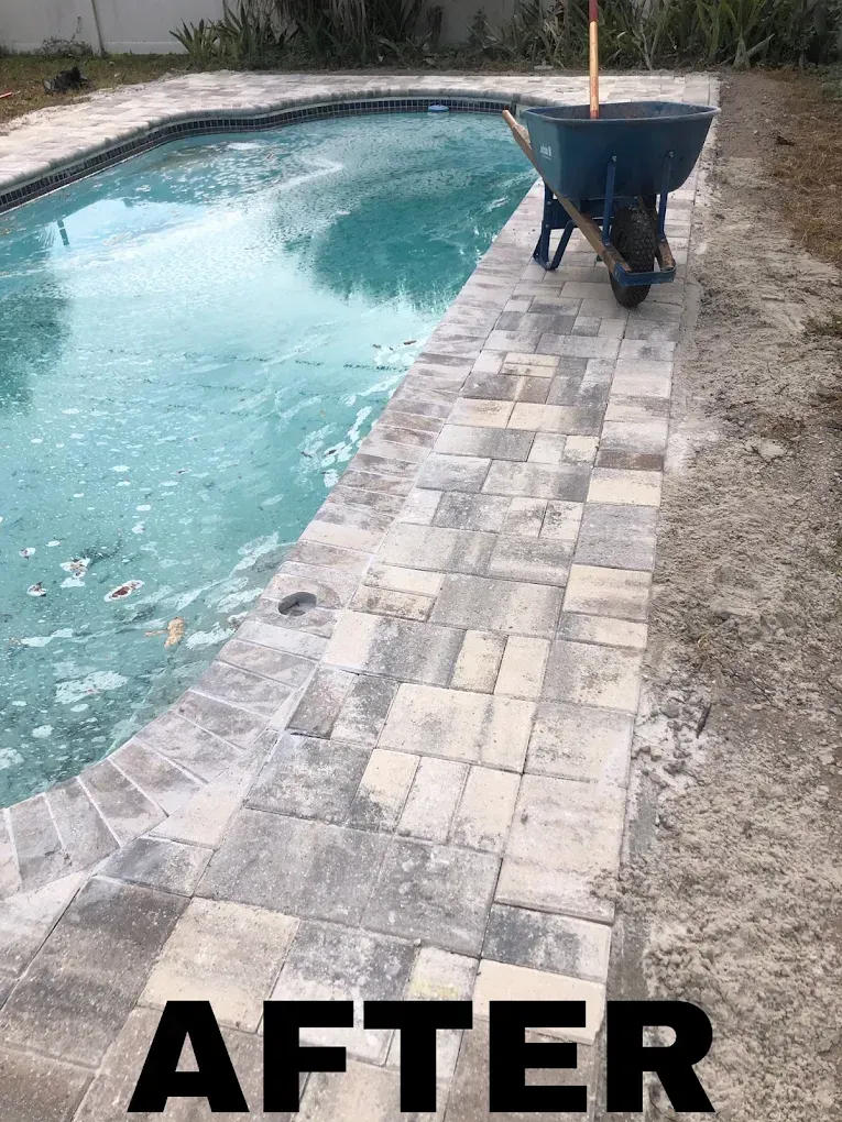 Poolside patio with newly laid pavers, turquoise water, and a wheelbarrow.