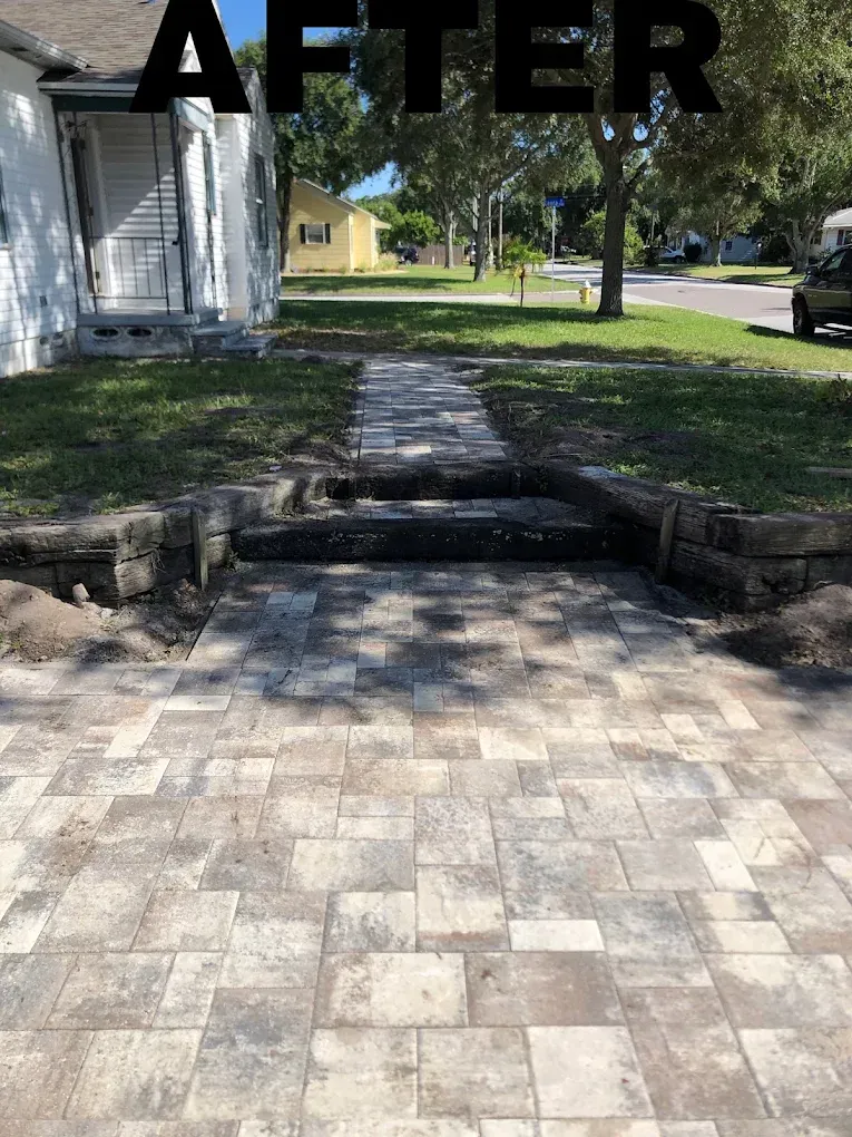 Newly paved stone pathway leading to a house with small retaining walls and steps in a grassy yard.