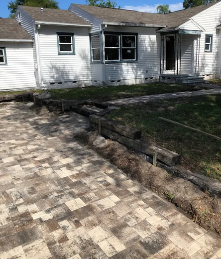 House with a brick driveway and a raised garden bed, construction in progress.