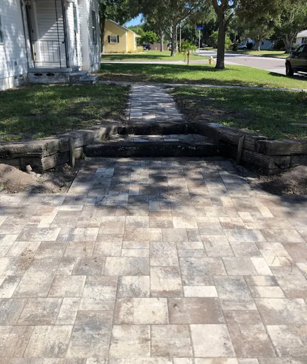 Stone pathway leading to a house with small retaining walls and steps. Green grass and trees are in the background.