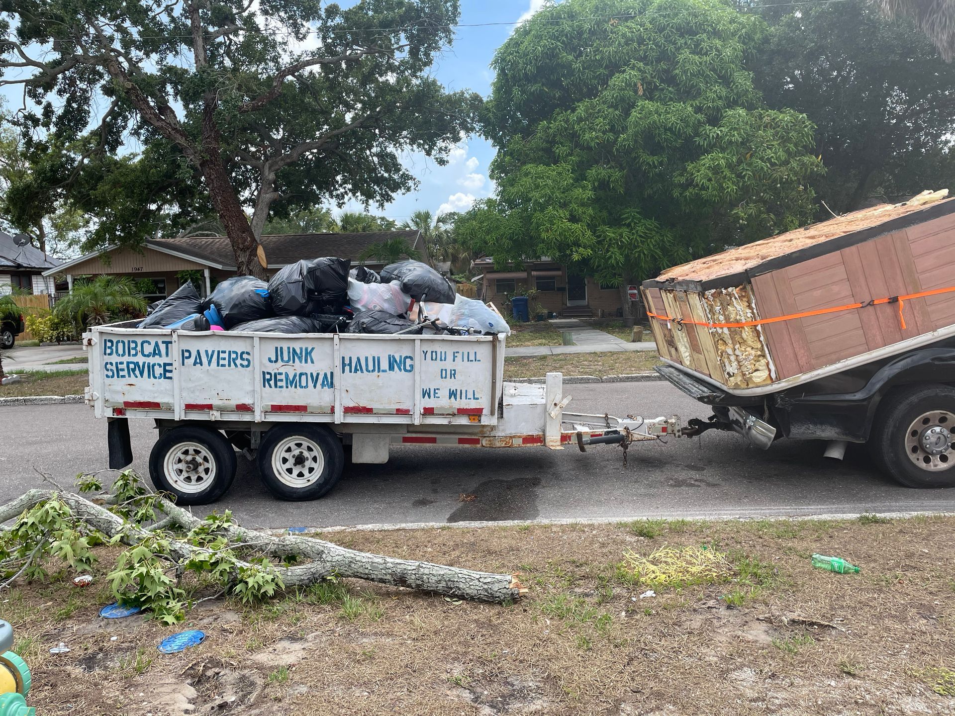 Truck towing trailer with junk and debris, parked on a street near a house.