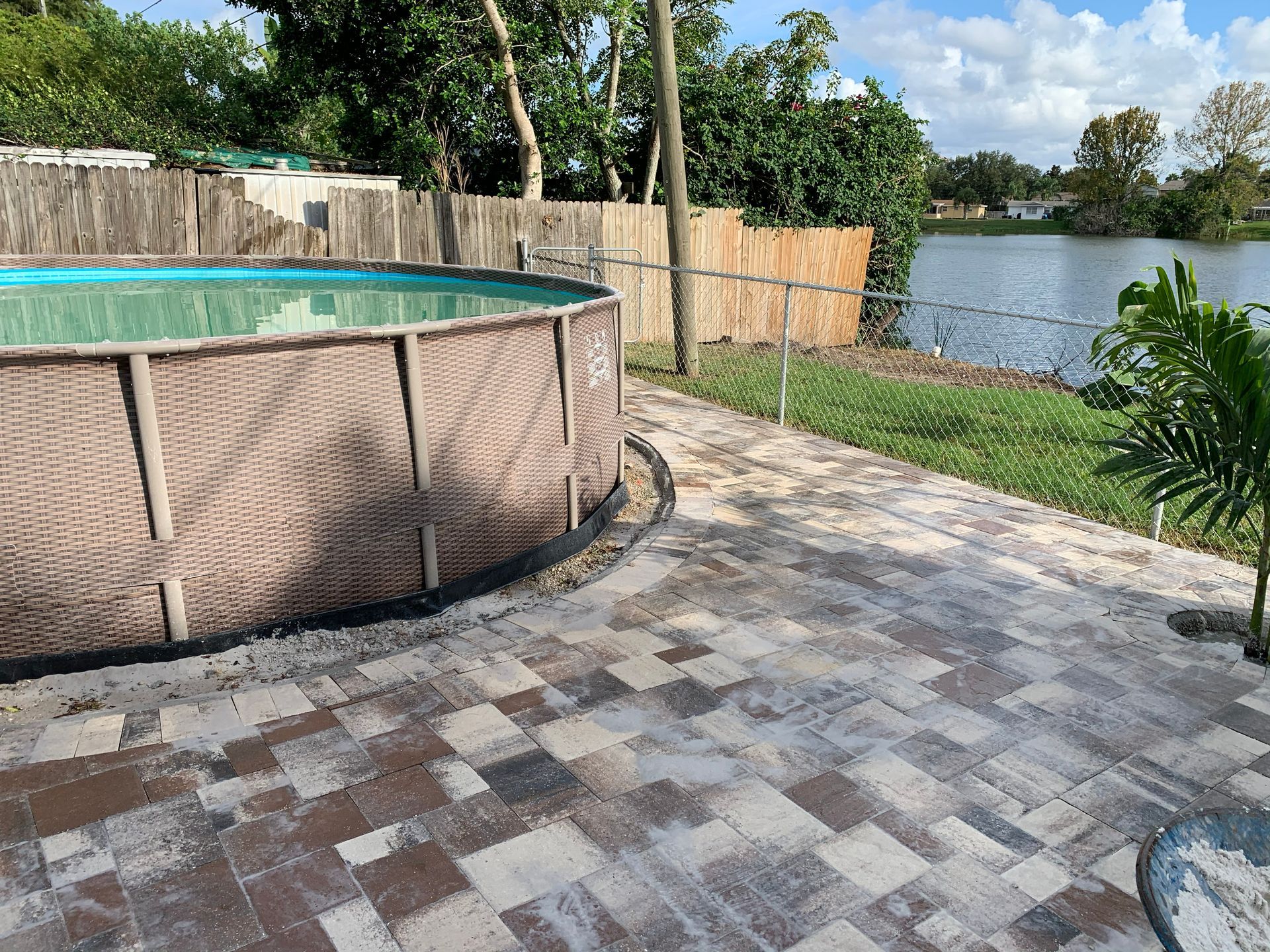 An above-ground pool next to a lake with a paver patio.
