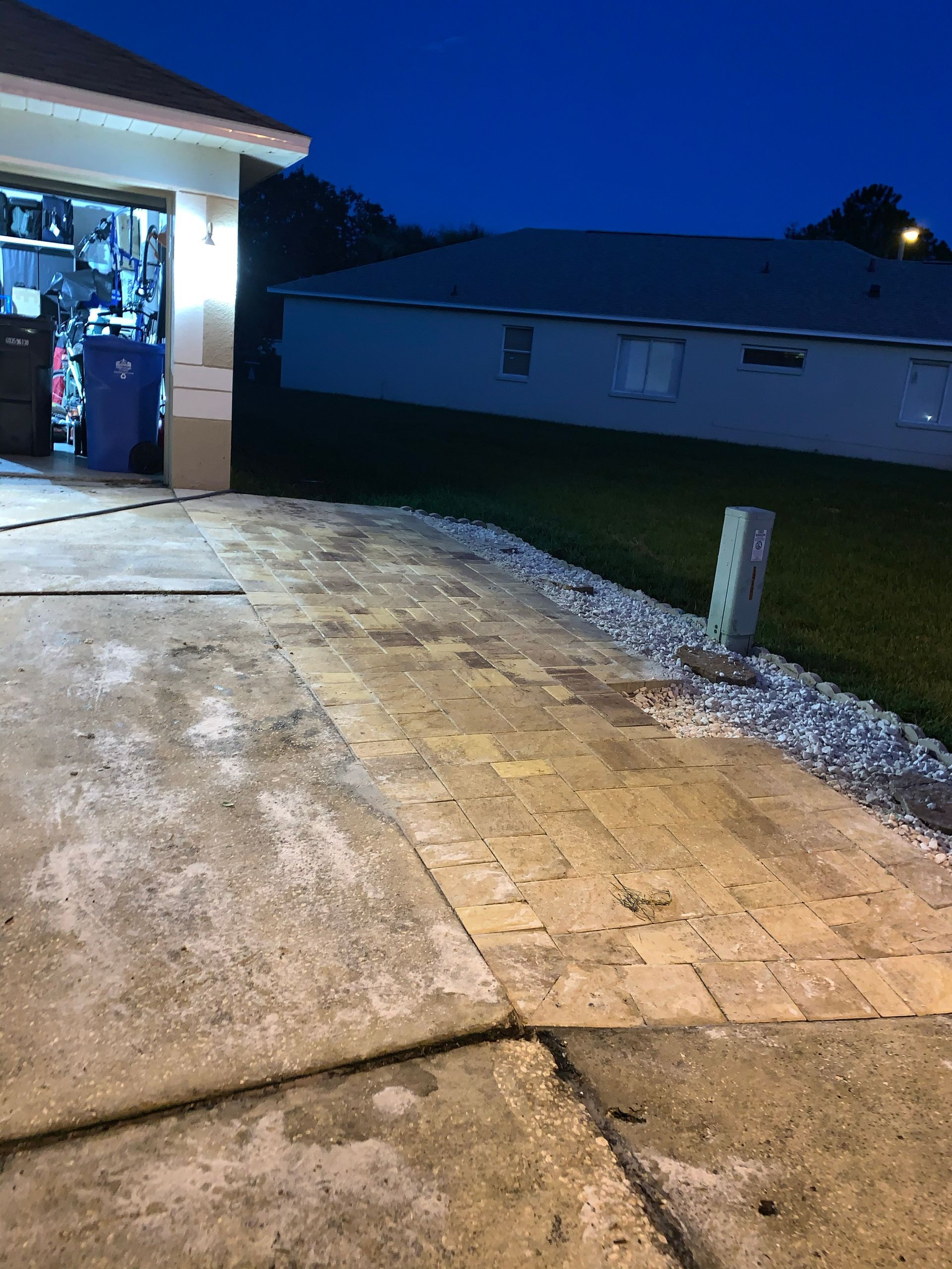Garage and driveway at dusk; light colored pavers and concrete; house in background.