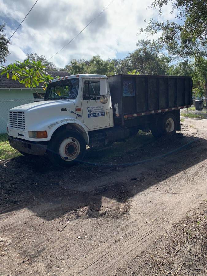 White dump truck parked on a dirt road, dark dump bed. Overcast sky.