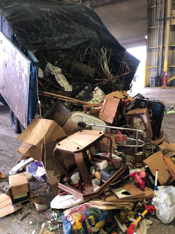 A garbage truck dumping trash in a waste facility. The pile contains cardboard, furniture, and plastic.