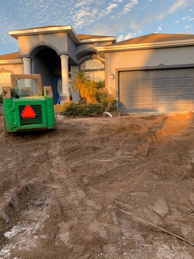 Green Bobcat construction vehicle on dirt in front of a blue house with a garage.