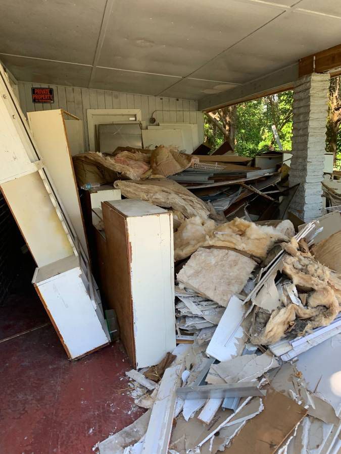 Pile of construction debris and cabinets on a porch, including insulation, wood, and drywall. Red floor.