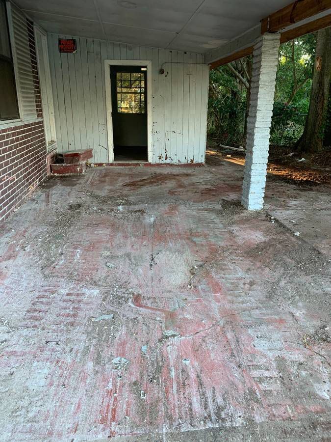 Covered porch with weathered red brick floor, white siding, and a door.